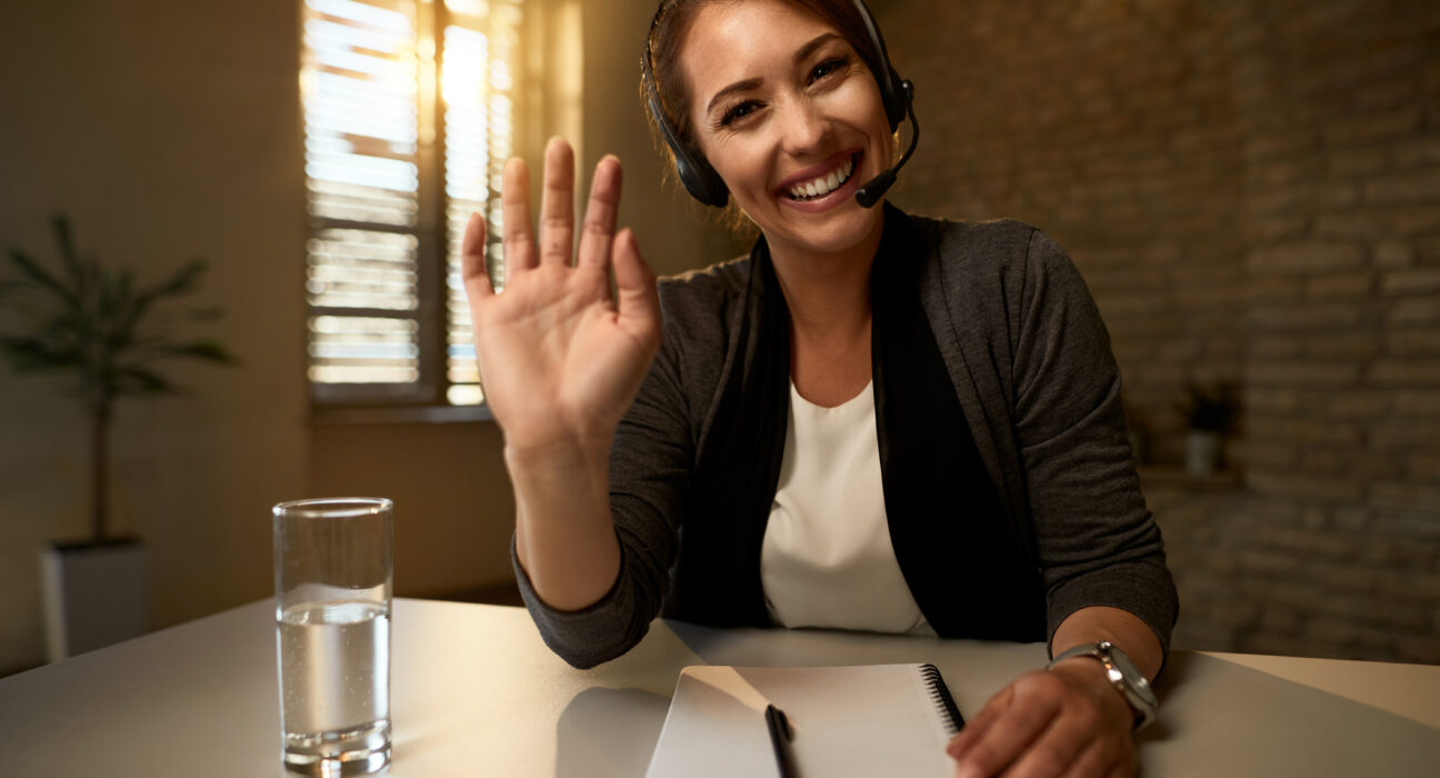 jovem-empresaria-feliz-usando-fone-de-ouvido-e-acenando-durante-videoconferencia-no-escritorio